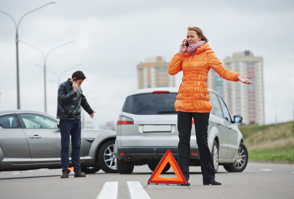 Man and woman on phone with car accident in the background