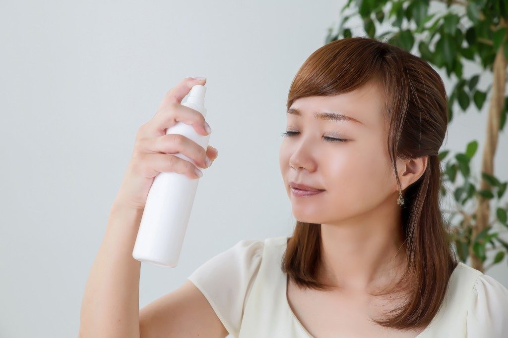 Asian woman spraying her face with skincare product