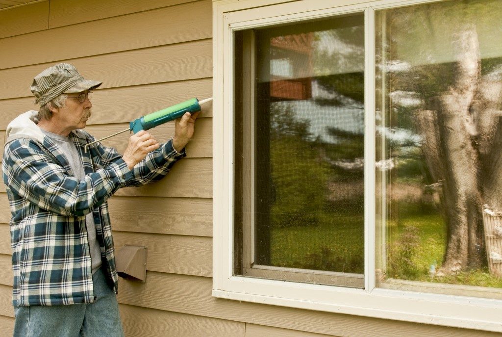 Workman sealing an exterior window with caulk to reduce air infiltration