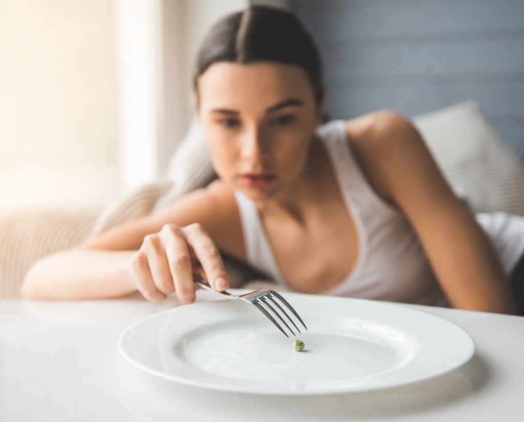 Suffering from anorexia. Girl is trying to put a pea on the fork