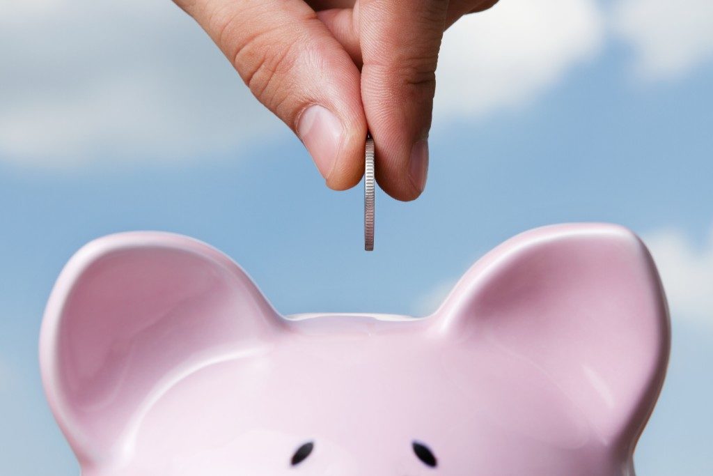 Saving, male hand putting a coin into piggy bank