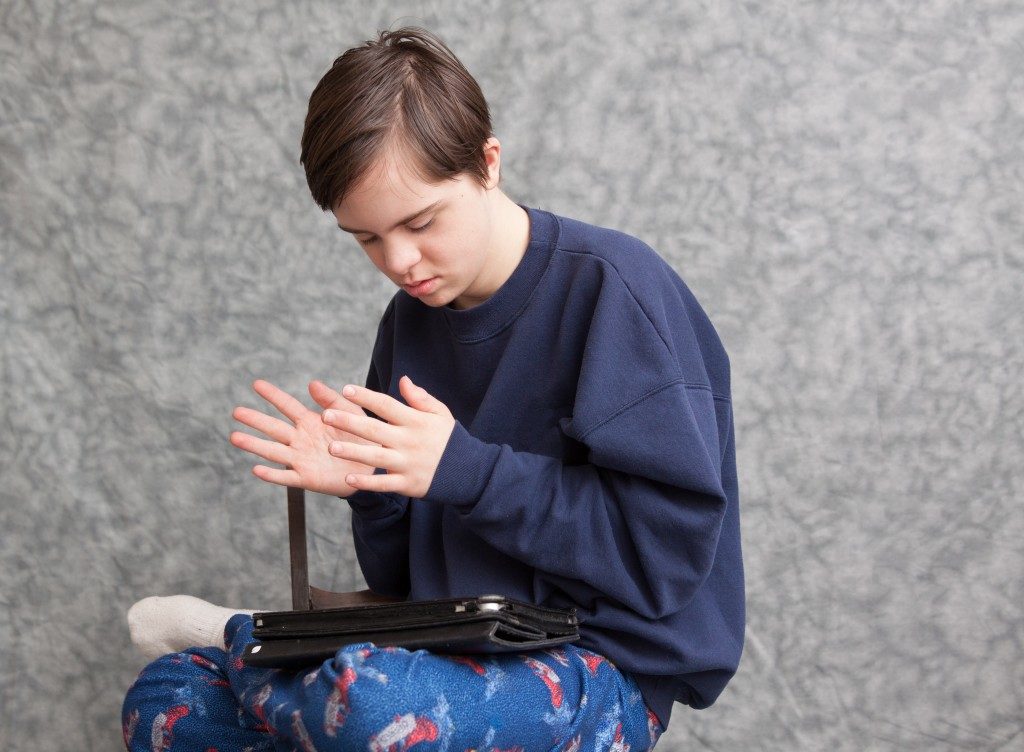 horizontal orientation of a boy with autism and down's syndrome clapping his hands as he plays with a tablet device / Apps for children with Autism