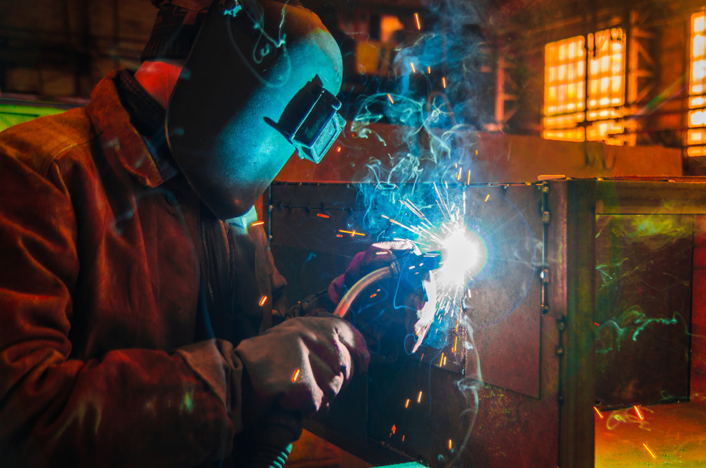 A welder wearing a welding mask and gloves uses a MIG gun on a metal surface